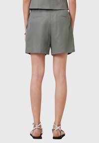 Pantaloni corti in lino verde con una vestibilità comoda, dotati di due tasche posteriori e una texture liscia. Abbinati a sandali argentati con cinturini.