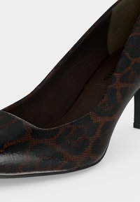 Chaussure à talon haut en cuir imprimé léopard marron et noir, bout pointu et talon fin noir sur fond blanc.
