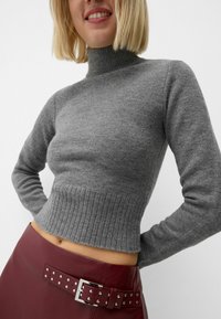 Szary dzianinowy sweter z golfem z prążkowanym dołem i długimi rękawami, zestawiony z bordową skórzaną spódnicą z paskiem ozdobionym ćwiekami.