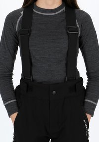 Pantalons de neige noirs avec bretelles noires réglables, dotés d'une fermeture à bouton, de poches latérales et d'un détail de logo blanc sur la jambe. Haut gris à manches longues en dessous.