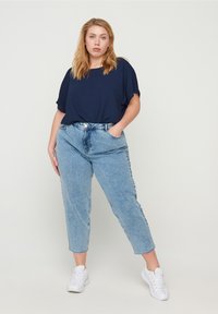 Un haut navy à manches courtes associé à un jean en denim taille haute de couleur bleu clair. Des baskets blanches complètent la tenue décontractée.