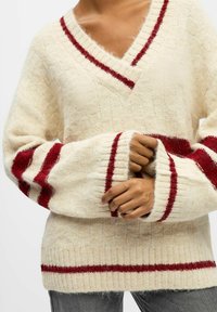 Crème sweater met een V-hals, rode gestreepte accenten op de mouwen en zoom, textuur stof en een losse pasvorm. Ideaal voor casual laagjes.