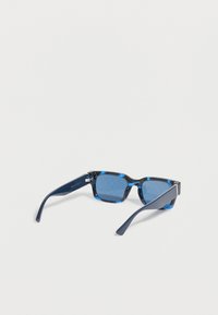 Gafas de sol rectangulares con tintado azul, montura marmoleada negra y azul y patillas curvas de color azul oscuro sobre un fondo blanco.