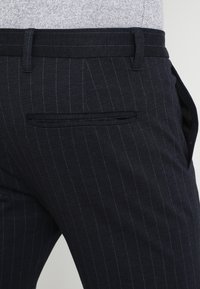 Mörkblå byxor med en finrandig mönster, som har en elegant design, sidofickor och en bakficka med ett diskret passepoil.