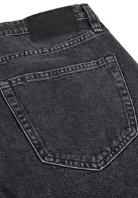 Los jeans de mezclilla negros cuentan con un bolsillo trasero con costuras visibles y una tela oscura y texturizada. Una etiqueta de cuero de la marca se encuentra en la cinturilla.