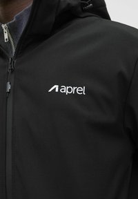 Sort vandtæt jakke med lynlås foran, justerbar hætte og et hvidt "aprel" logo på brystet. Glat, mat tekstur.
