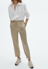 Pantalons beiges slim-fit avec poches latérales, associés à une chemise blanche à boutons et des baskets claires. Texture lisse avec un design ajusté.
