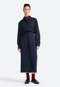 Abito a righe navy con bottoni, colletto, maniche lunghe e vita con cintura; abbinato a calzini bordeaux e mocassini.