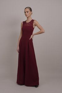 Burgundski kombinezon s prilegajočim korpusom, čipkastim detajlom na izrezu in širokimi, nabranimi hlačnicami. Gladek material in eleganten silhuet.