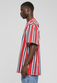 Röd, marinblå och vit randig kortärmad t-shirt, avslappnad passform, med rund halsringning och sidofickor, bärs med ljusblå jeans.