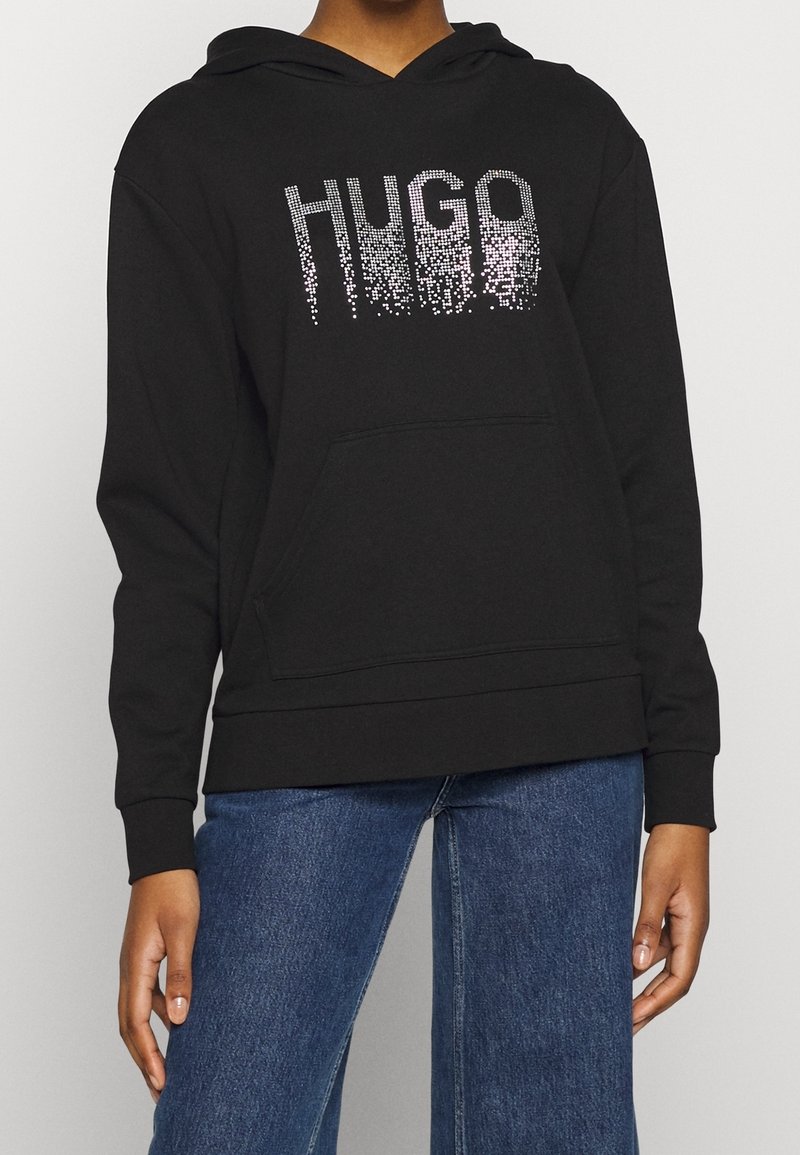 Czarna bluza z kapturem, z przednią kieszenią, z gradientowym kropkowanym logo "HUGO" w białym kolorze. Materiał wydaje się miękki i ma luźny krój.