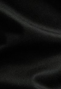 Närbild av svart tyg med fin vävtextur och subtila veck som skapar mjuka skuggor och höjdpunkter.