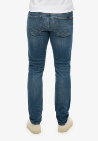 Jeans de mezclilla azul deslavados con un diseño ajustado, estilo de cinco bolsillos y detalles de costura sutiles. Llevados con zapatos de color claro.