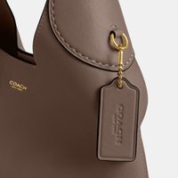 Sac à main en cuir marron Coach avec quincaillerie dorée et étiquette en cuir fixée embossée « COACH New York ».