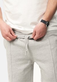 Graue Sweatpants mit einem elastischen Bund und einer Zugkordel, mit Seitennähten und einem weichen, strukturierten Stoff. Hände, die den Bund anpassen.
