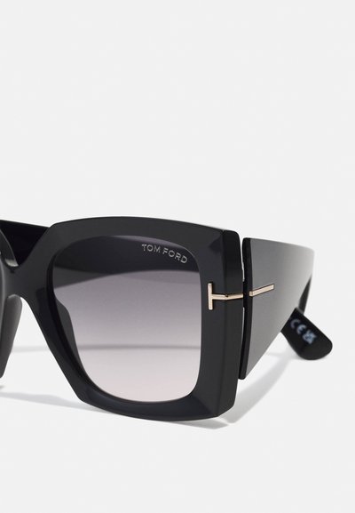 Occhiali da sole oversize neri con lenti sfumate. Presentano un design geometrico, dettagli in metallo dorato e un logo Tom Ford prominente.