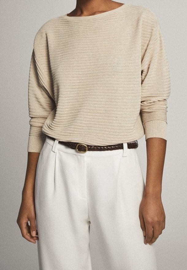 Maglione beige a coste con scollo ampio e maniche lunghe, abbinato a pantaloni bianchi e una cintura intrecciata marrone.