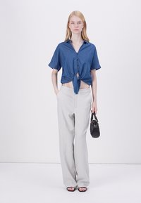 Denim korte mouw overhemd met een knoopdetail in de taille, gecombineerd met lichtgrijze wijde broek en een kleine zwarte handtas.