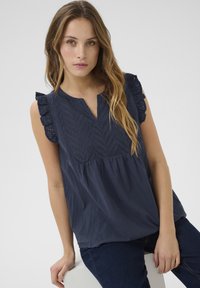Blouse bleu marine avec un col en V, motif à pois et manches volantées. Fabriquée en tissu léger avec une coupe ample et un ourlet froncé.