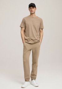 Beżowa bawełniana koszulka z krótkim rękawem i okrągłym dekoltem, w połączeniu z dopasowanymi beżowymi spodniami dresowymi. Uzupełniona białymi trampkami i czapką w kolorze czarnym.