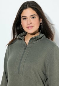 Oliwkowy sweatshirt z półzamkiem i teksturowanym materiałem, o luźnym kroju. Posiada subtelne detale szycia z przodu.