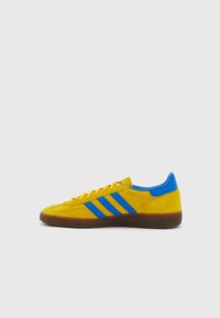 Zapatillas de ante en un brillante color amarillo con detalles en azul, que presentan tres rayas azules, cordones planos y una suela de goma marrón.