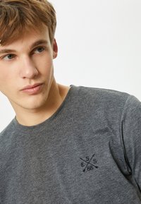 Grå kortærmet t-shirt lavet af bomuld med rund halsudskæring, med et broderet logo på venstre bryst i sort.