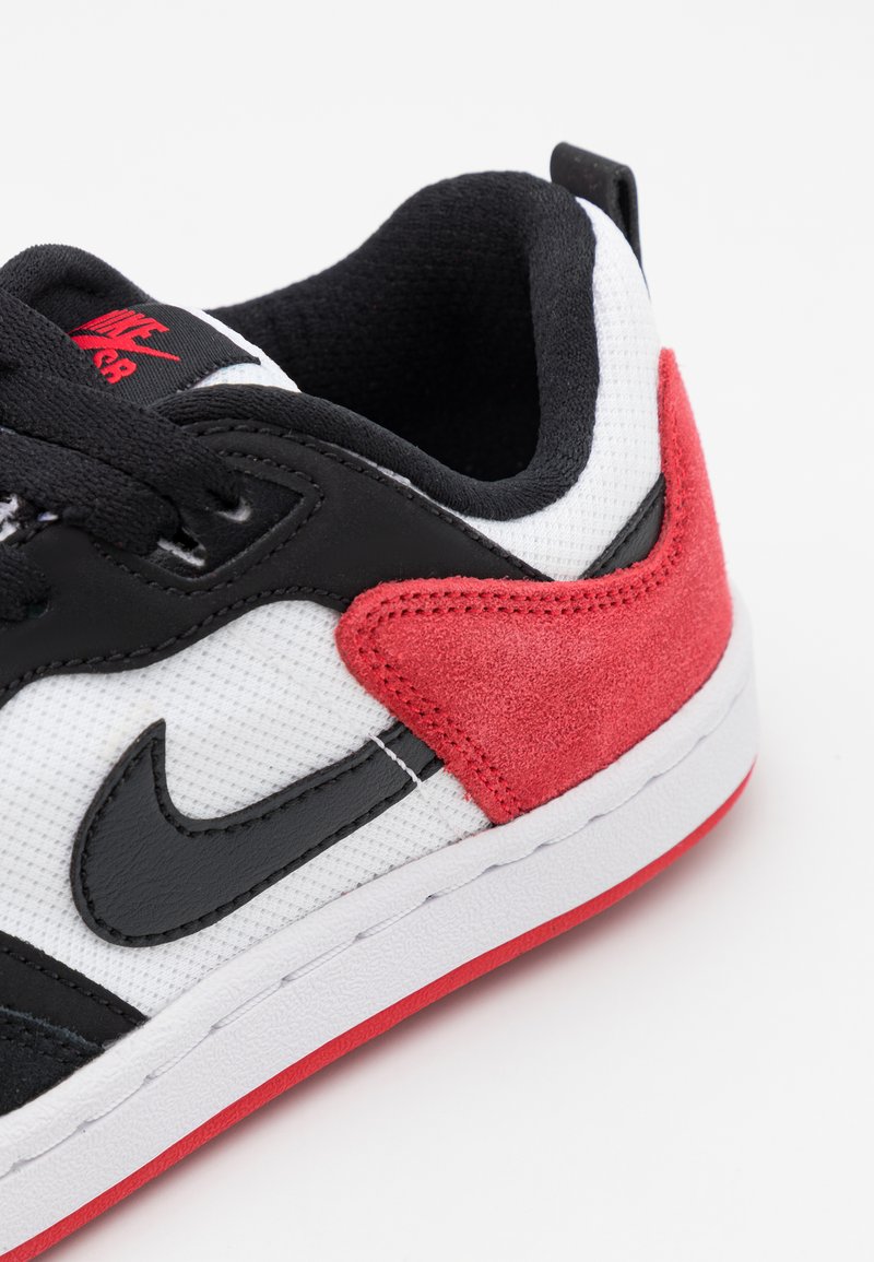 Czarno-białe sneakersy z czerwonymi zamszowymi akcentami, teksturowana siateczkowa cholewka, czarne logo Swoosh oraz biała podeszwa środkowa z czerwoną podeszwą.