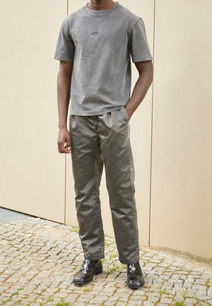 T-shirt en coton gris avec un logo embossé subtil, associé à un pantalon texturé gris et des chaussures en cuir noir avec des détails du logo.