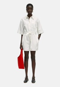 Witte katoenen jurk met een strik taille en korte mouwen, gecombineerd met een rode tote bag en zwarte flats. Gladde stof, minimalistisch ontwerp.
