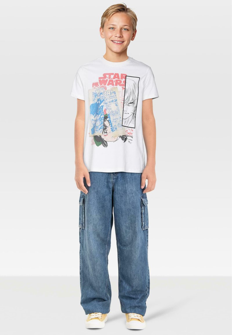Λευκό βαμβακερό t-shirt με πολύχρωμο σχέδιο "Star Wars" και τέχνη σε στιλ κόμικ. Συνδυασμένο με φαρδιά μπλε τζιν cargo παντελόνια και κίτρινες αθλητικές sneakers.