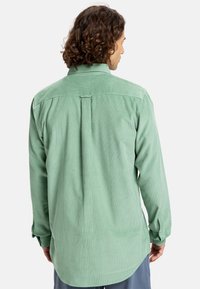 Groene corduroy overhemd met lange mouwen, een kraag met knopen en een rugplooi. Heeft knoopsluiting bij de manchetten en een gebogen zoom.