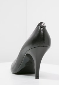 Escarpins en cuir noir à talon haut avec un bout pointu et une texture lisse. Présente un accent décoratif en argent au niveau du talon.