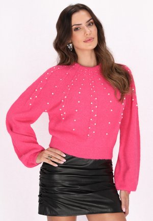 Roze gebreide trui met parelversieringen, ronde halslijn en ballonmouwen, gedragen met een zwarte gerimpelde mini-jurk.
