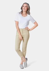 Witte korte mouwen t-shirt gecombineerd met beige slim-fit broek, met een ritsdetail aan de voorkant en zilveren veterschoenen. Eenvoudig ontwerp en neutrale kleuren.