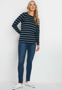 Långärmad topp i marinblått och blå horisontella ränder, ihop med blå skinny jeans och vita sneakers. Mjuk tyg med avslappnad passform.