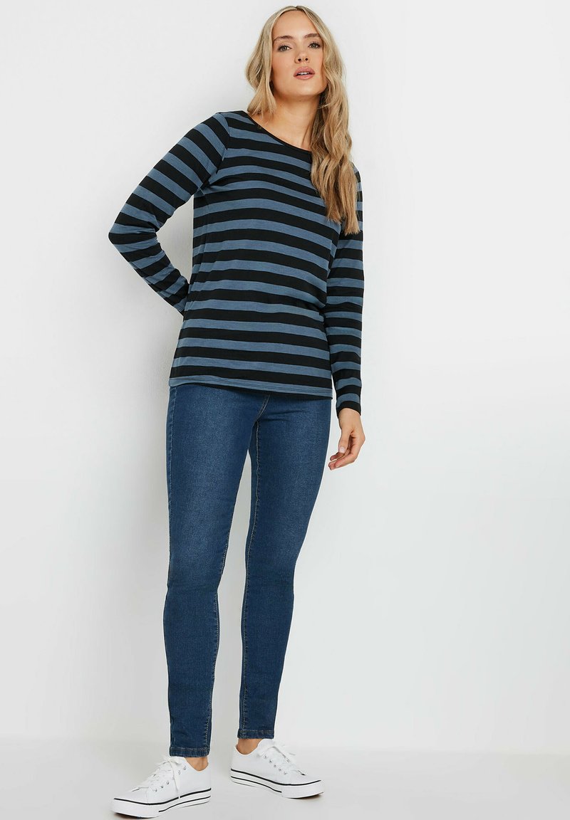 Långärmad topp i marinblått och blå horisontella ränder, ihop med blå skinny jeans och vita sneakers. Mjuk tyg med avslappnad passform.