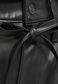 Czarna skórzana odzież związana w talii i detalem w postaci guzików. Tekstura jest gładka, z widocznymi szwami wzdłuż krawędzi.