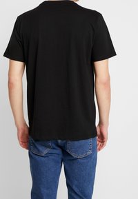 Sort bomulds t-shirt med korte ærmer og en klassisk rund halsudskæring. Bagfra ses en lige snit og en glat tekstur. Parret med blå jeans.