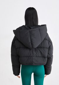 Chaqueta de plumas negra con capucha, que presenta un diseño acolchado y un largo corto. La textura suave y los puños elásticos realzan las mangas.