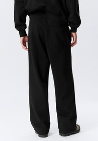 Black sweatpants with a relaxed fit, elastic waistband, and a single back pocket. Soft texture with a smooth finish and loose legs.