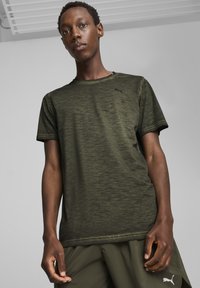 Camiseta deportiva de manga corta en color verde oliva, con una textura suave y un sutil patrón jaspeado. Presenta un pequeño logo negro de Puma en el pecho.
