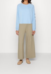Jasnoniebieski skrócony sweatshirt z długimi rękawami, w zestawieniu z beżowymi spodniami o szerokich nogawkach. Beżowe, teksturowane buty wsuwane dopełniają całość.