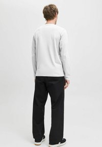 Camisa blanca de manga larga con escote redondo, combinada con pantalones anchos negros. El fondo es liso y de color claro.