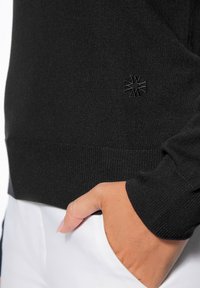Czarny sweter wykonany z dzianiny, z ribbowym wykończeniem u dołu i na mankietach. Posiada małe, wytłoczone logo po lewej stronie u góry.