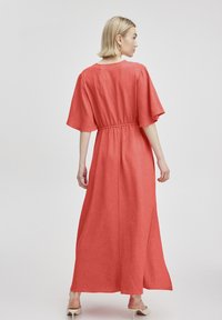 Korallenfarbenes Maxikleid mit kurzen, weiten Ärmeln und elastischem Taillenbund. Hergestellt aus strukturiertem Stoff, bietet es eine lockere Passform und ein bodenlanges Design.