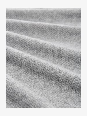 Šviesiai pilka medžiaga su smulkia tekstūra, kurioje yra minkštos raukšlės ir šiek tiek margas raštas, vaizduojantis jaukumą ir šilumą.