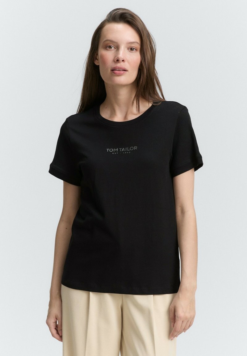 Zwarte katoenen t-shirt met korte opgerolde mouwen en ronde halslijn, voorzien van een klein grijs "TOM TAILOR" logo afgedrukt op de voorkant.