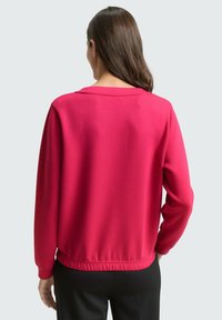 Aangesloten lange mouw top in levendig fuchsia, gemaakt van een gladde stof. Voorzien van een ronde hals en elastische zoom voor een getailleerde pasvorm.