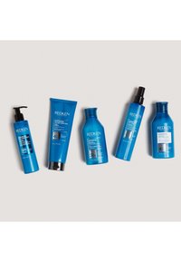 Fem Redken hårvårdsprodukter i blå flaskor: en pumpflaska, en tub och tre flaskor i olika former, alla med produktetiketter.